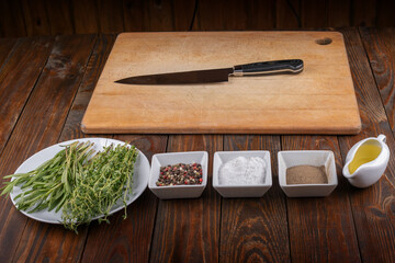Chopping board, seasonings and rosemary on dark wooden background.