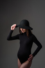 Young beautiful pregnant woman in black bodysuit and hat.