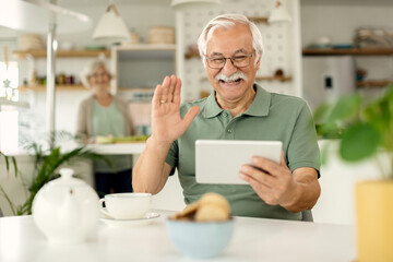 Happy mature man waving while having video call over digital tablet at home.