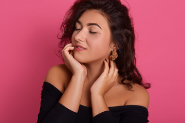 Portrait of cute lovely girl wearing black outfit with dark wavy hair, posing with closed eyes isolated on pink background, attractive lady full of dreams.