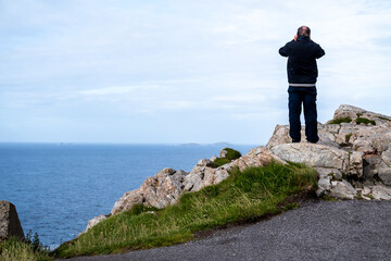 Aged man standing on the cliff using binoculars