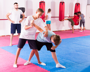 Naklejka na ściany i meble Children working in pair mastering new self defence moves during group class with male coach