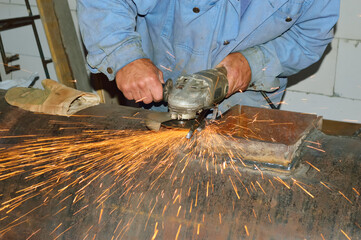 close-up - work with an iron boiler, a worker cuts a small narrow strip of iron with a grinder, hot bright sparks fly