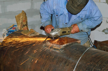 close-up - work with an iron boiler, a worker in special clothes cuts iron with a grinder, hot bright sparks fly