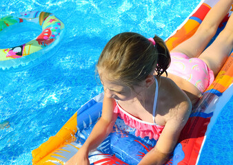 close-up - a girl in a pink swimsuit swims on an inflatable mattress in the pool, next to her is an...
