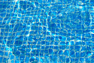 blue mosaic pool bottom filled with water, bright reflections and small waves on the surface