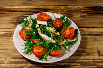 Tasty salad of fried chicken breast, fresh arugula and cherry tomatoes on wooden table