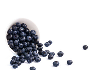 Blueberries in a white ceramic bowl spilled out. On a white background, isolated on white.