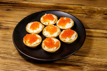 Tartlets with red caviar and soft cheese on a wooden table