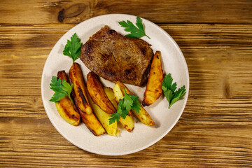 Fried beef steak with potato wedges on wooden table. Top view