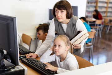 Fototapeta na wymiar Young female teacher working with schoolgirl in computer class of school library