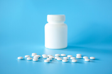 White plastic pill bottle with white teblets pills on blue background with selective focus