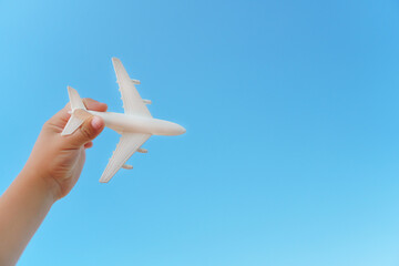 A white airplane in a child's hand against a blue sky. The concept of a dream of travel and flights.