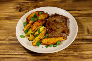 Fried beef steak with potato wedges on wooden table