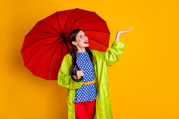 Portrait of her she nice attractive lovely cheerful cheery glad fashionable girl wearing green raincoat holding raindrop on palm isolated bright vivid shine vibrant yellow color background