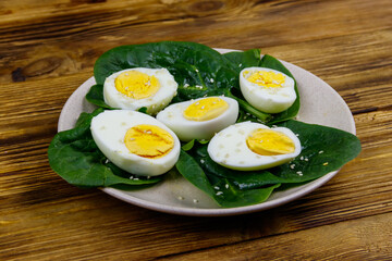Boiled eggs with fresh spinach leaves and sesame seeds on wooden table