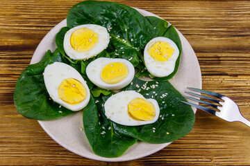 Boiled eggs with fresh spinach leaves and sesame seeds on wooden table. Top view