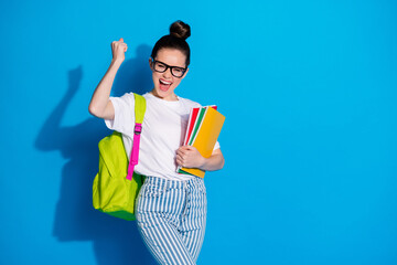 Portrait of crazy ecstatic girl hold many books copybooks backpack enjoy extra lecture courses win lottery raise fists scream yes wear white denim isolated bright shine color background