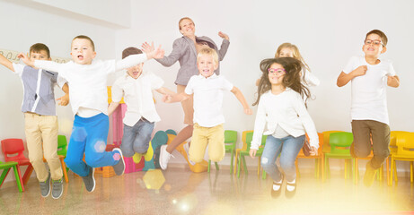 Obraz premium Group of happy cheerful children with their female teacher jumping together in a schoolroom