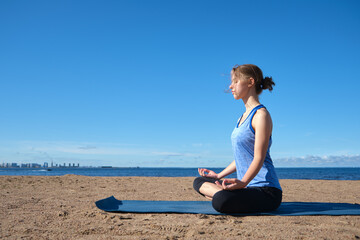 Fototapeta na wymiar Young slim girl doing yoga, lotus position on the beach, relaxation and meditation