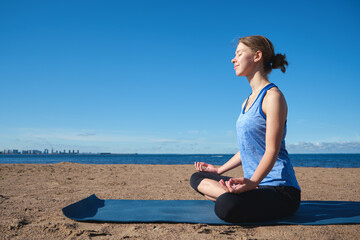 Naklejka na ściany i meble Young slim girl doing yoga, lotus position on the beach, relaxation and meditation
