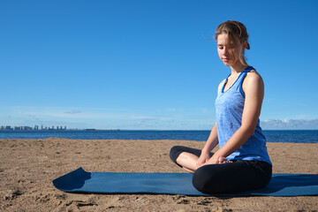 Naklejka na ściany i meble Young slender girl doing yoga on the beach on a sunny morning, sad mood, sad thoughts