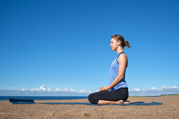 Young slim girl doing yoga, lotus position on the beach, relaxation and meditation