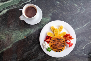 pancake topping with banana ice cream and strawberry on Mable table with hot drink.