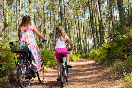 cute little girl and her mom riding a bicycle in a pine forest