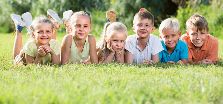 smiling kids lying on green grass on bright summer day