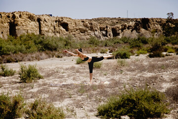 Young active woman practicing yoga in desert on sunny day, health and active life concept