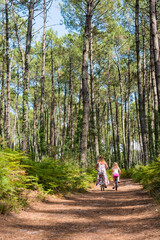 cute little girl and her mom riding a bicycle in a pine forest