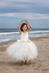 Fototapeta na wymiar Dance on the beach.A beautiful little girl in a white ballet dress walks and dances on a sandy beach