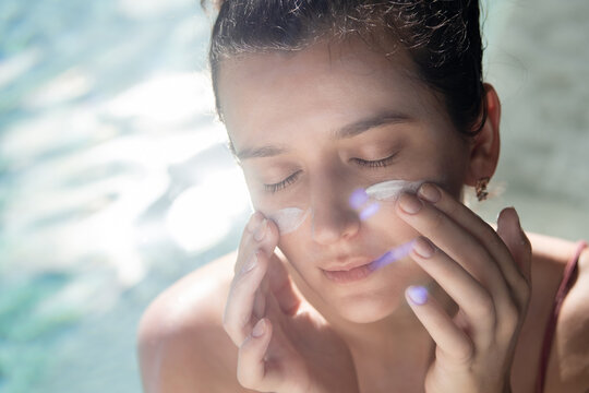Woman applying sunscreen sunblock on face outdoors by pool under sunshine. Summer skin care