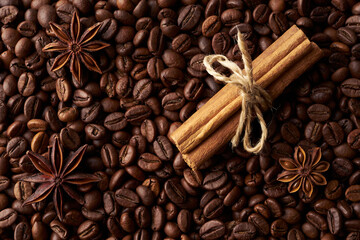 Tied cinnamon sticks and anise on a heap of roasted whole coffee beans