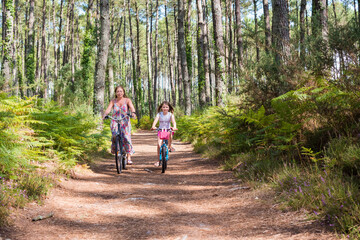cute little girl and her mom riding a bicycle in a pine forest