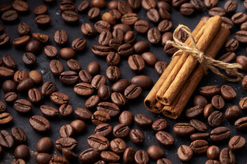 Roasted whole coffee beans and tied sticks of cinnamon on a dark background