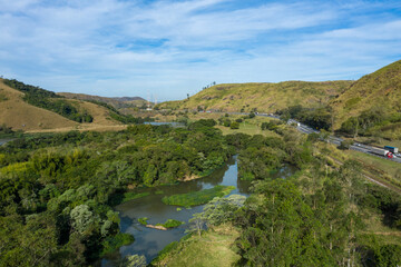 Highway with river and train road. Aerial landscape view of a scenic road in the valley surrounded by the beautiful Brazilian Mountains. 