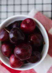 Top down view of a bowl of juicy red cherries sat on top of a red and white napkin and a dark black cooling rack.  Food concept macro fruit photo
