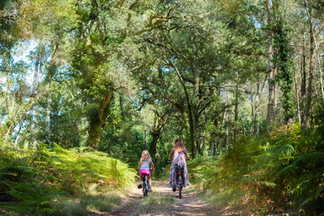 Obraz premium cute little girl and her mom riding a bicycle in a pine forest