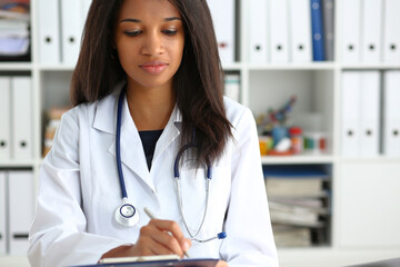 Beautiful smiling black female doctor hold clipboard pad and fill something with silver pen. Physical illness prevention prescribe remedy ward round therapeutist assistance healthy lifestyle concept