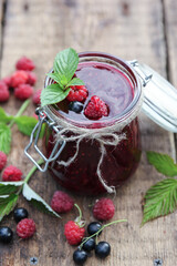 Berry jam in a jar. Preservations. Black currant and raspberry jam, fresh mint, leaves on an old wooden table. Rustic. Background image, copy space, vertical