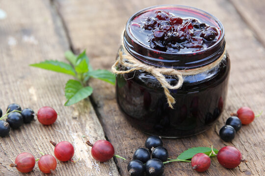 Berry jam in a jar. Preservations. Black currant and gooseberry jam, fresh mint and chamomile on an old wooden table. Rustic. Background image, copy space, horizontal