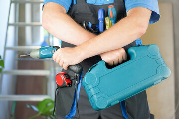 Builder guy holds a toolbox and a cordless screwdriver