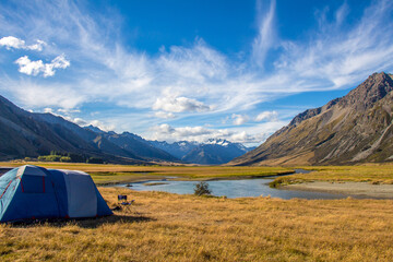 A tent pitched beside a river, surrounded by mountains, in New Zealand
