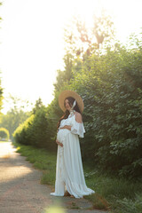 Fototapeta premium Pregnant woman posing in a white dress on a background of nature.