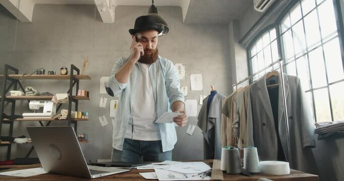 Cool hipster designer working in his office, talking or recording voice message on phone, making an order, customer service - fashion, small business concept 4k footage