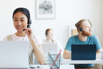 Asian smiling operator in headset working at her workplace at office