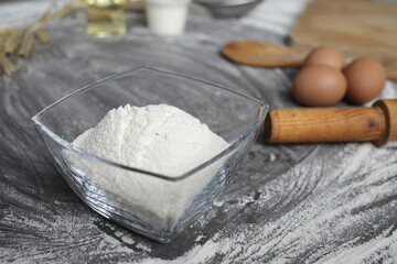 Flour, egg, olive oil, milk, wheat ears, kitchen tool on gray table background.