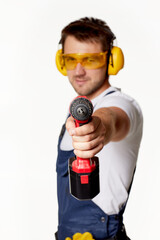 caucasian repairman worker in uniform, safety glasses and headphones holding cordless screwdriver isolated on white studio background. focus on cordless screwdriver